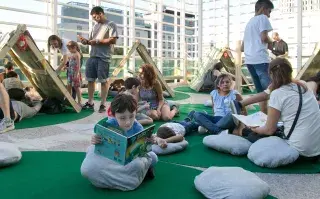 Niños leyendo libros en un parque con libros gigantes en el centro cultural de la ciencia
