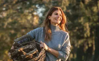 Juliana Awada adelantó, desde el sur, una de las prendas que será tendencia en el otoño 2025 Juliana Awada lleva un sueter gris y un canasto con troncos de madera en el campo