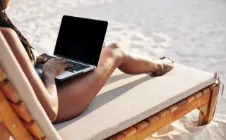 Tu negocio en vacaciones: 4 claves para hacer una pausa estratégica y potenciar resultados Una mujer en la playa con una laptop sobre las piernas.