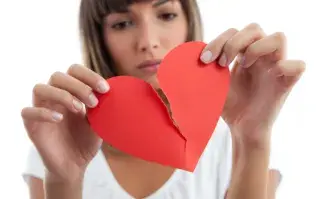 Foto de mujer rompiendo corazón de papel.