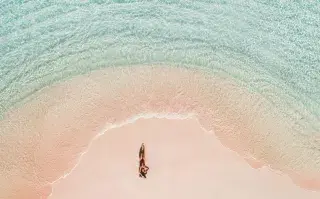 Una mujer tomando sol en una playa de arena rosa