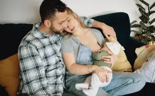 una mujer le da el pecho a su bebés y el marido acompaña