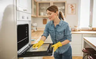 Ni vinagre ni bicarbonato: el truco casero para eliminar la grasa del horno en pocos pasos Una mujer limpiando el horno