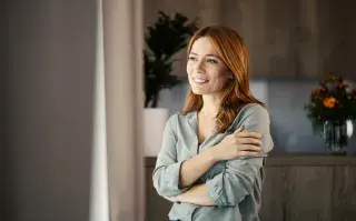 una mujer que mira por la ventana y piensa en proyectos futuros con alegría