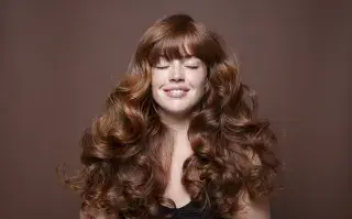 Pelo con rulos: los consejos de un estilista para hidratar, definir y controlar el frizz Una mujer con rulos con los ojos cerrados