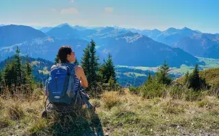 Mujer sentada con una mochila en los hombros contemplando el paisaje montañoso.