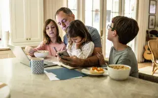 Pantallas a la hora de comer: cómo afectan los vínculos entre padres e hijos según la Psicología padres con chicos en la mesa con computadora y teléfono