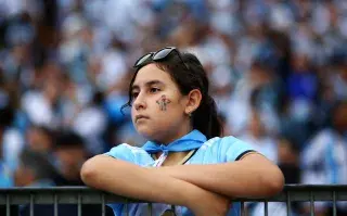 Mujer joven mirando partido de fútbol con la cara pintada de Messi