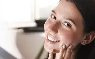 Una mujer tocándose la cara y sonriendo a la cámara