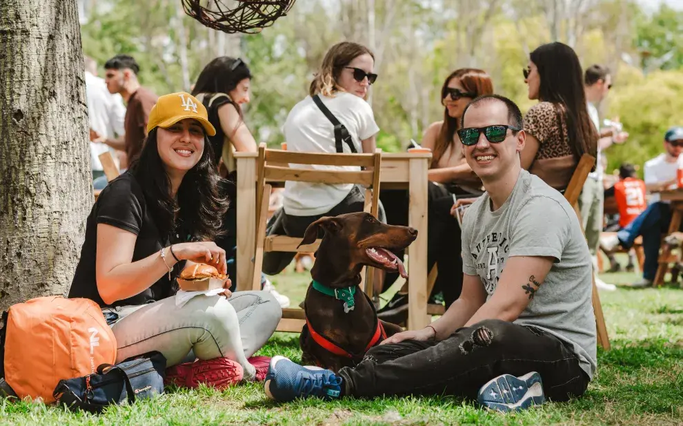 Chica y chico sentados en el pasto en un picnic, con un perrito.