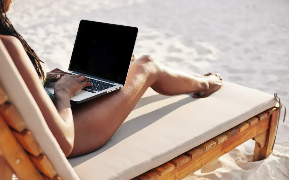 Una mujer en la playa con una laptop sobre las piernas.