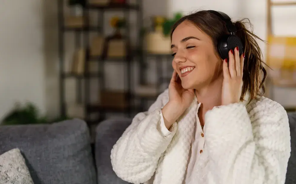 Una mujer escuchando musica desde sus auriculares en el sillón de su casa