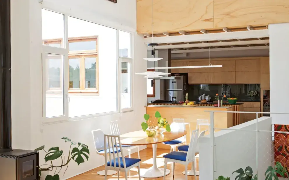 Un pequeño desnivel refuerza la transición entre el living y el comedor, con mesa 'Tulip' con tapa ovalada de madera y sillas con tapizado azul que combinan el modelo 'Tulip' con otras tipo Windsor. En primer plano, asiento tallado en madera del escultor Jorge Michel.