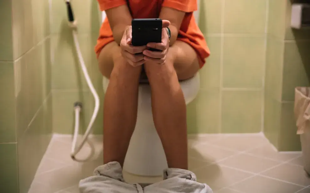 Una mujer sentada en el inodoro con un celular en la mano.