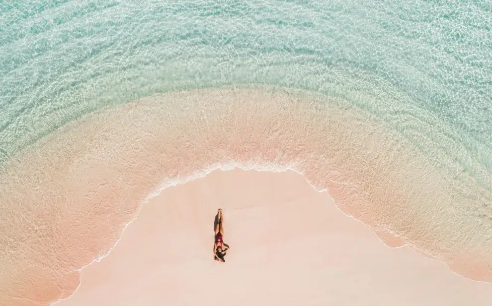 Una mujer tomando sol en una playa de arena rosa